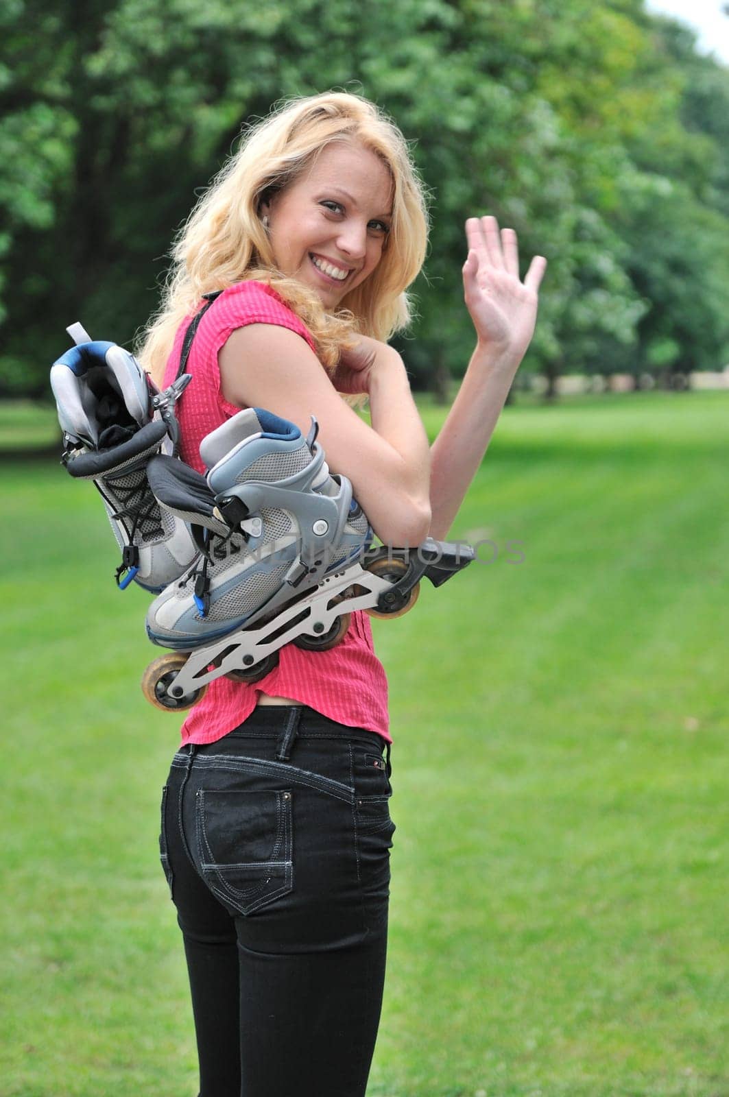 Young smiling woman with rollerskates giving good bye gesture with hand. Outdoors in park.
