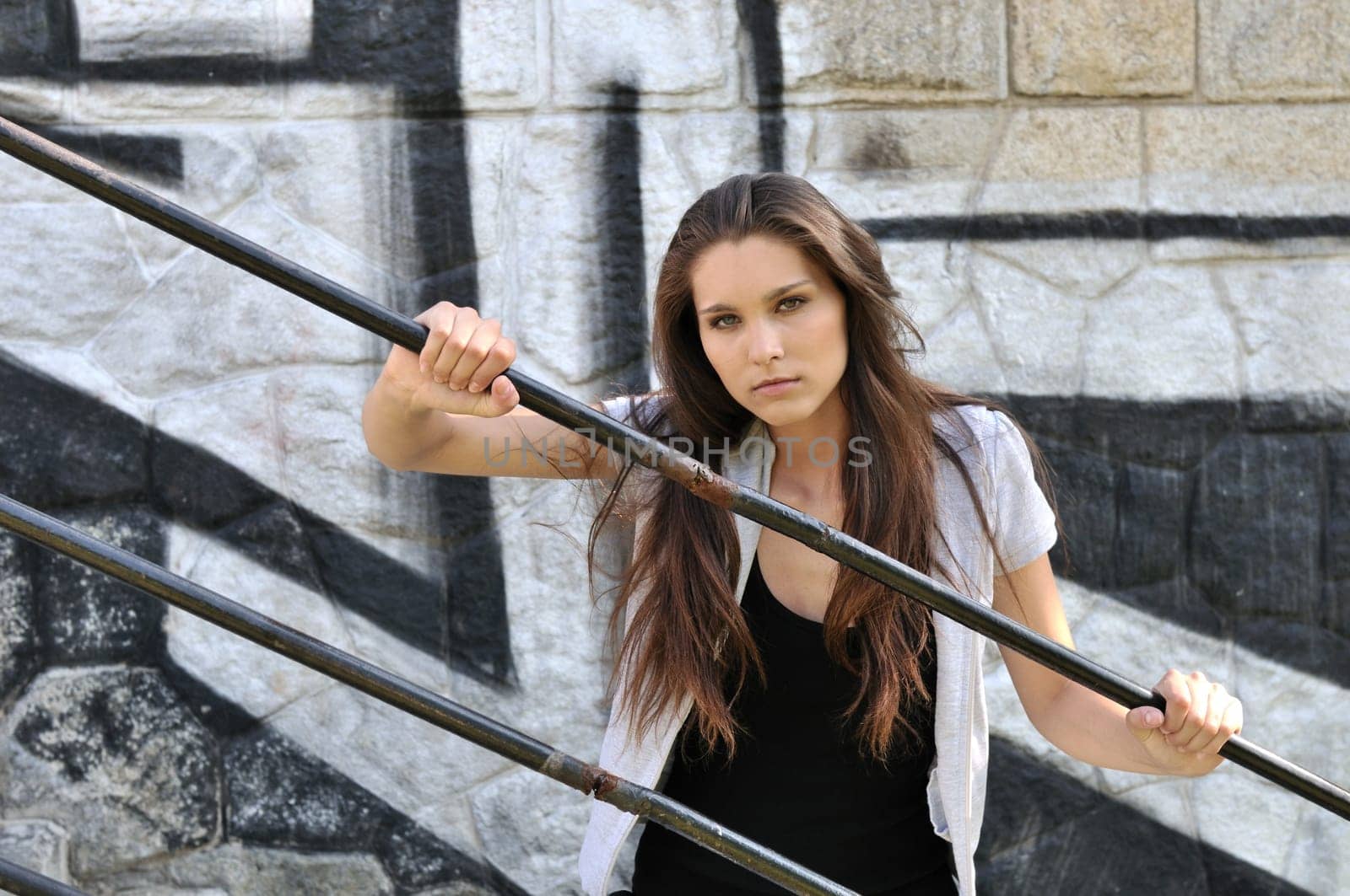 Young cool woman (teenage girl) portrait holding rail in front of black and white graffity wall
