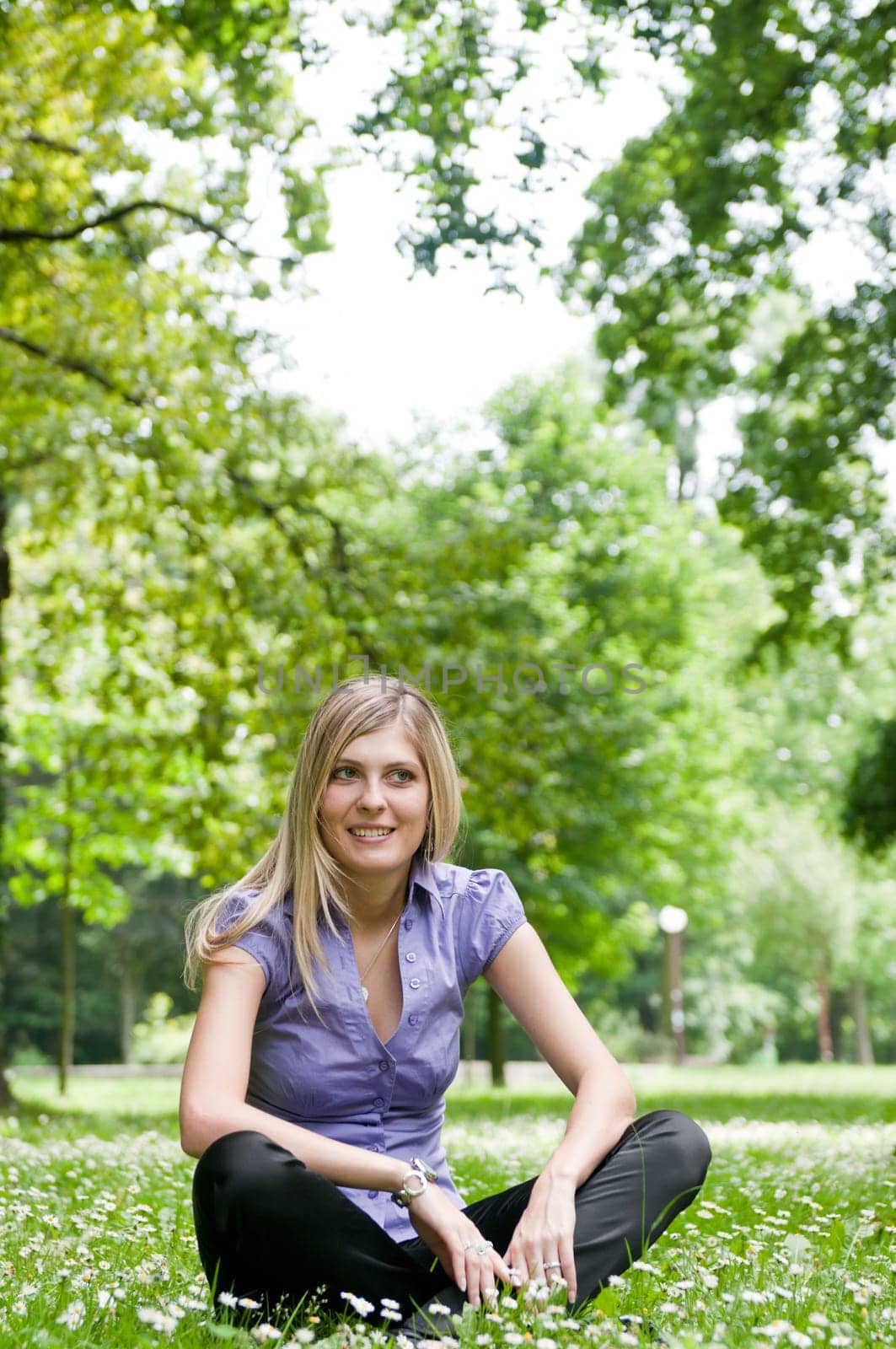 Young smiling woman siting in grass with flowers - outdoors scene