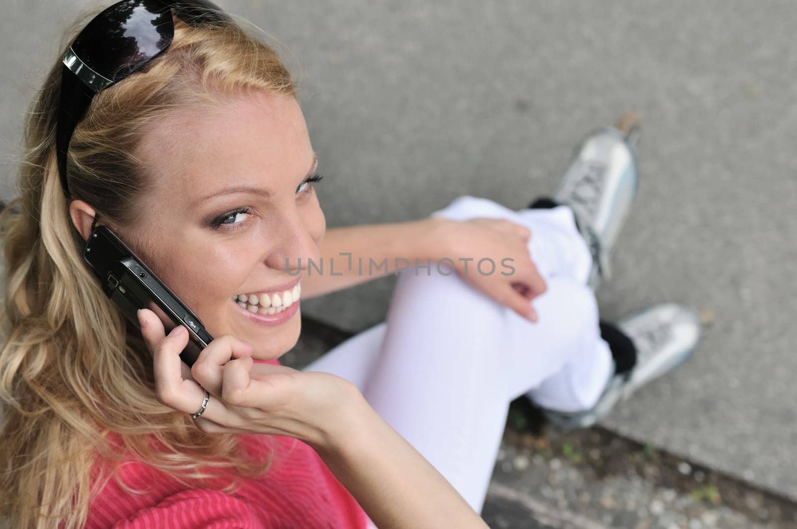 Young smiling woman wearing rollerblades calling with mobilephone outdoors