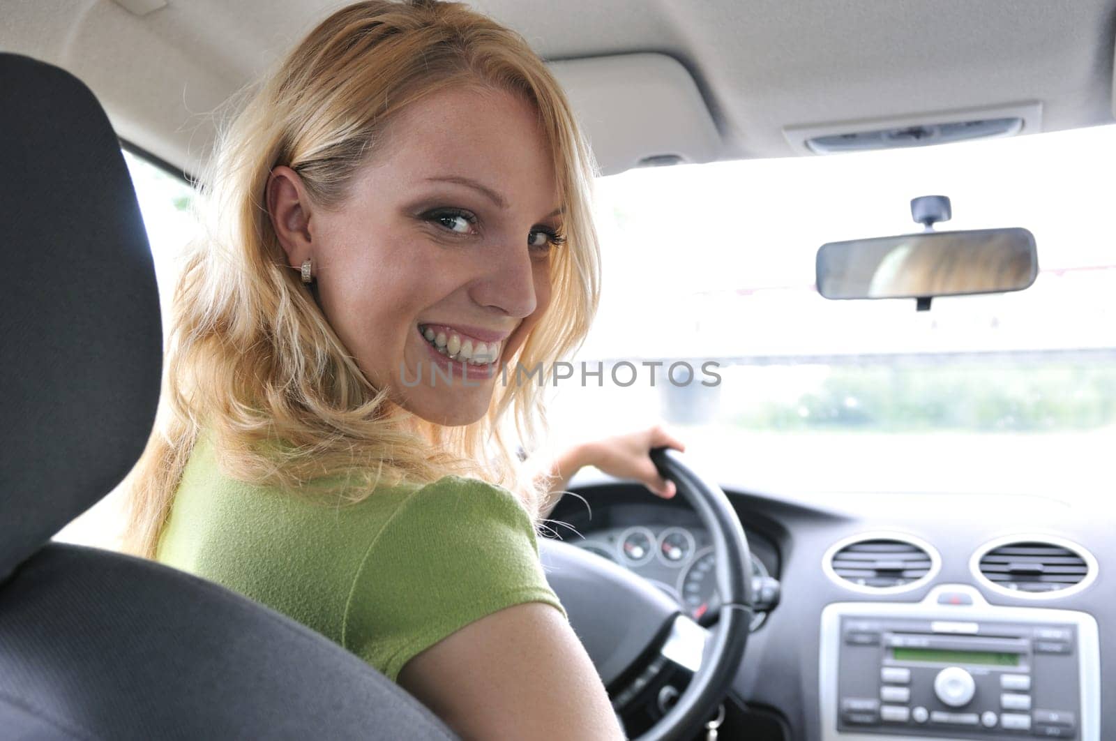 Portrait of young smiling woman siting behind steering wheel inside car