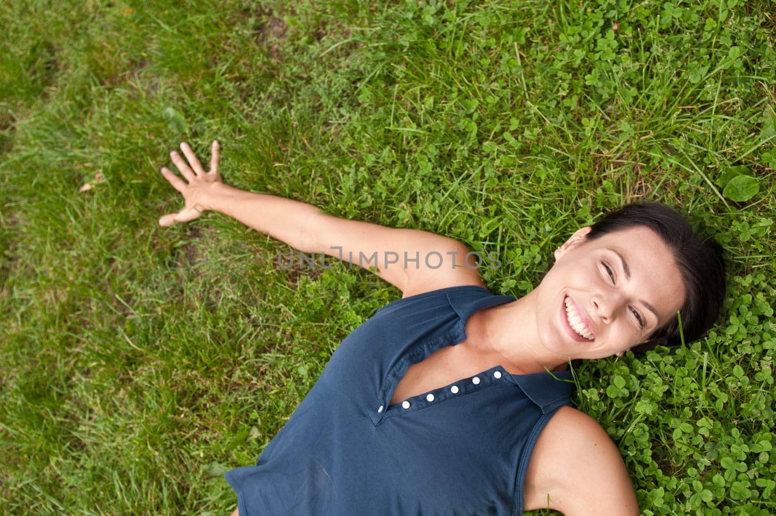 Young happy smiling woman lying in fresh green grass - above view