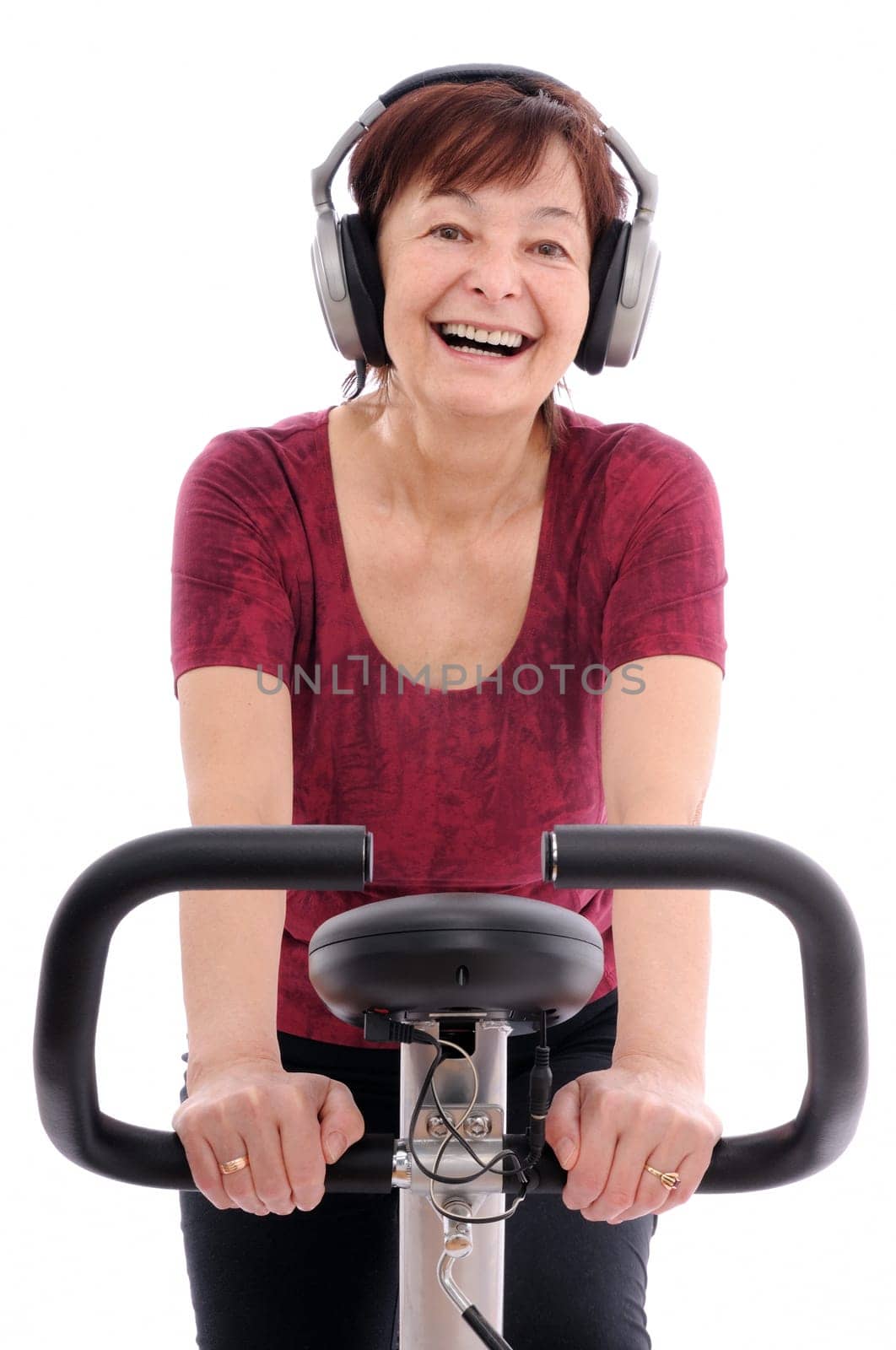 Senior woman with headphones listening music on spinning bicycle