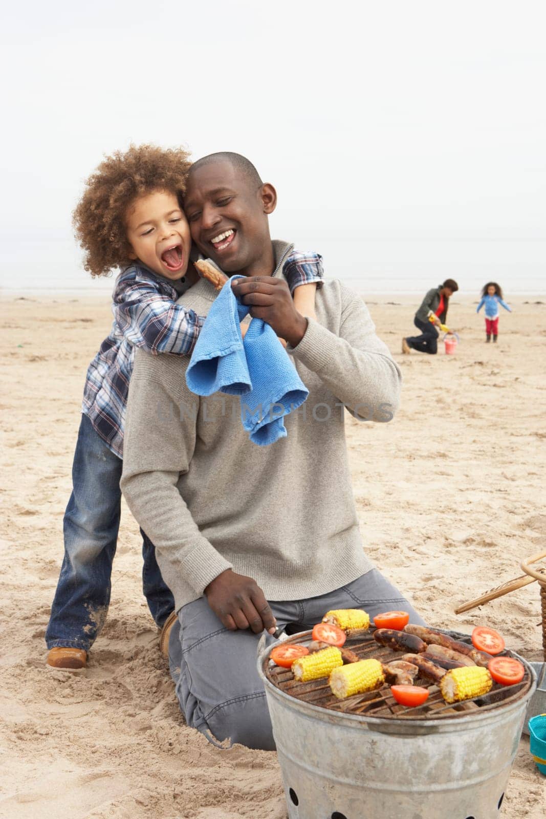 Young Family Enjoying Barbeque On Beach