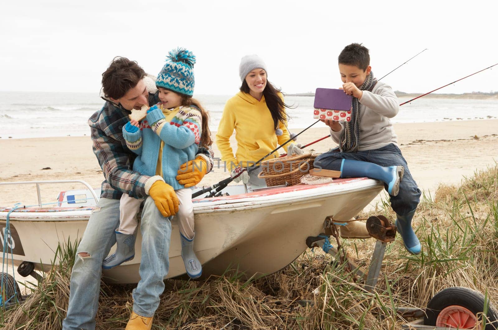 Family Group Sitting On Boat With Fishing Rod On Winter Beach