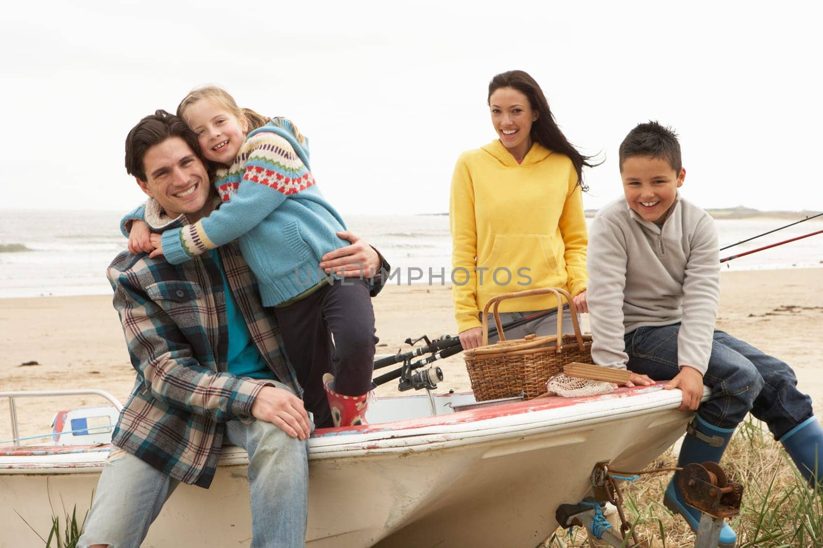 Family Group Sitting On Boat With Fishing Rod On Winter Beach