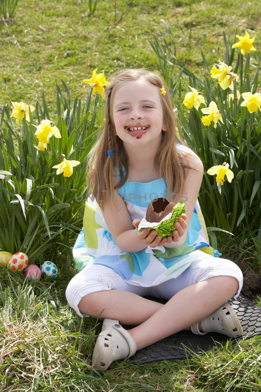 Girl Eating Chocolate Egg On Easter Egg Hunt In Daffodil Field