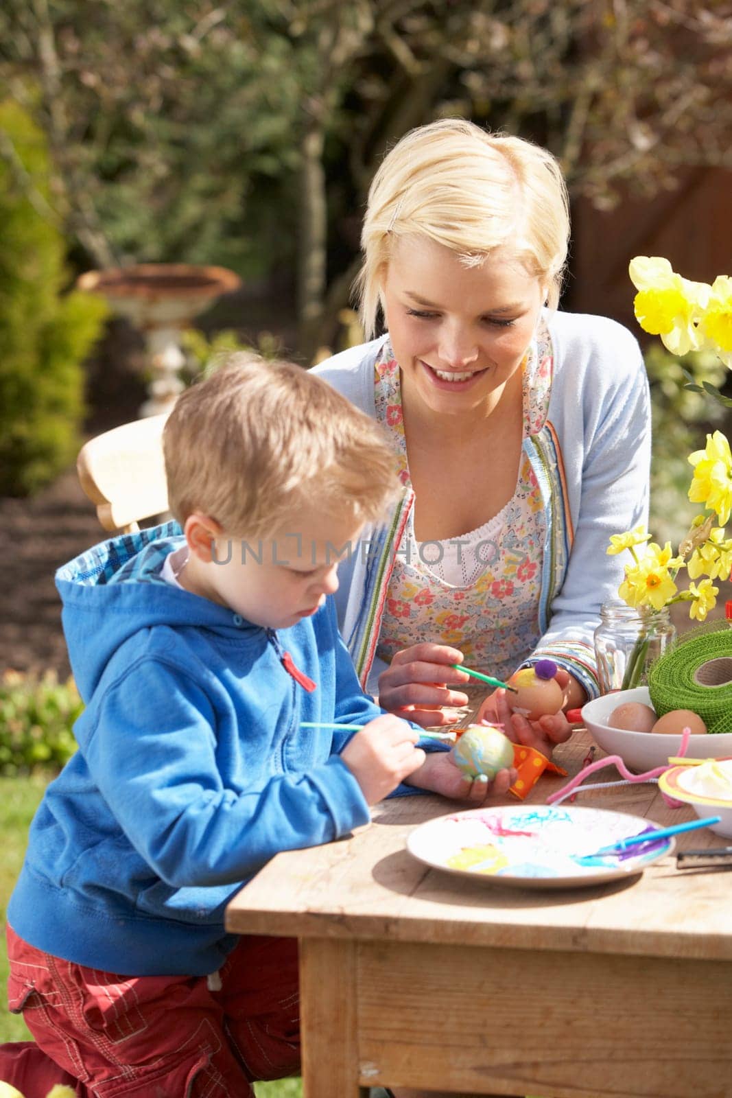 Mother And Son Decorating Easter Eggs On Table Outdoors