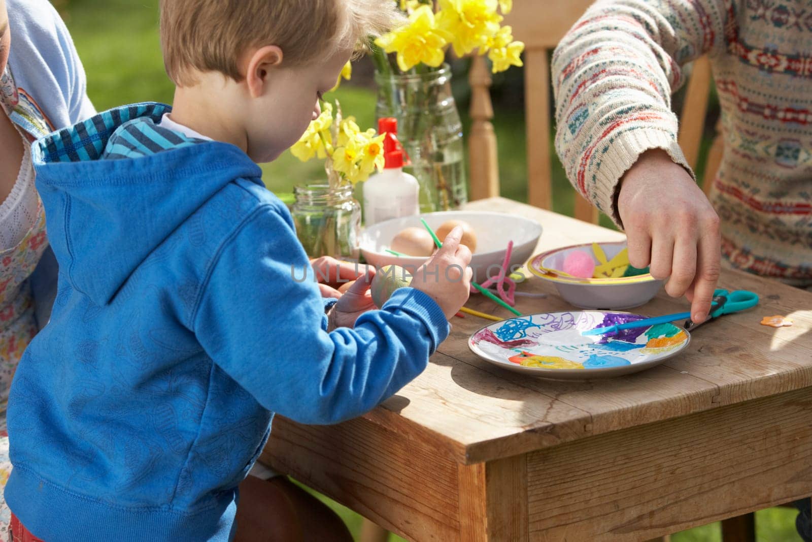 Father And Son Decorating Easter Eggs On Table Outdoors