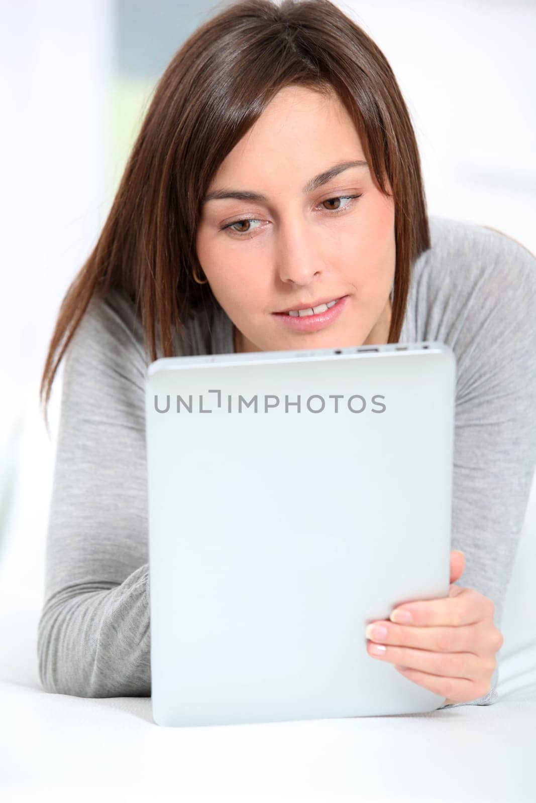 Young woman laying on sofa with electronic pad