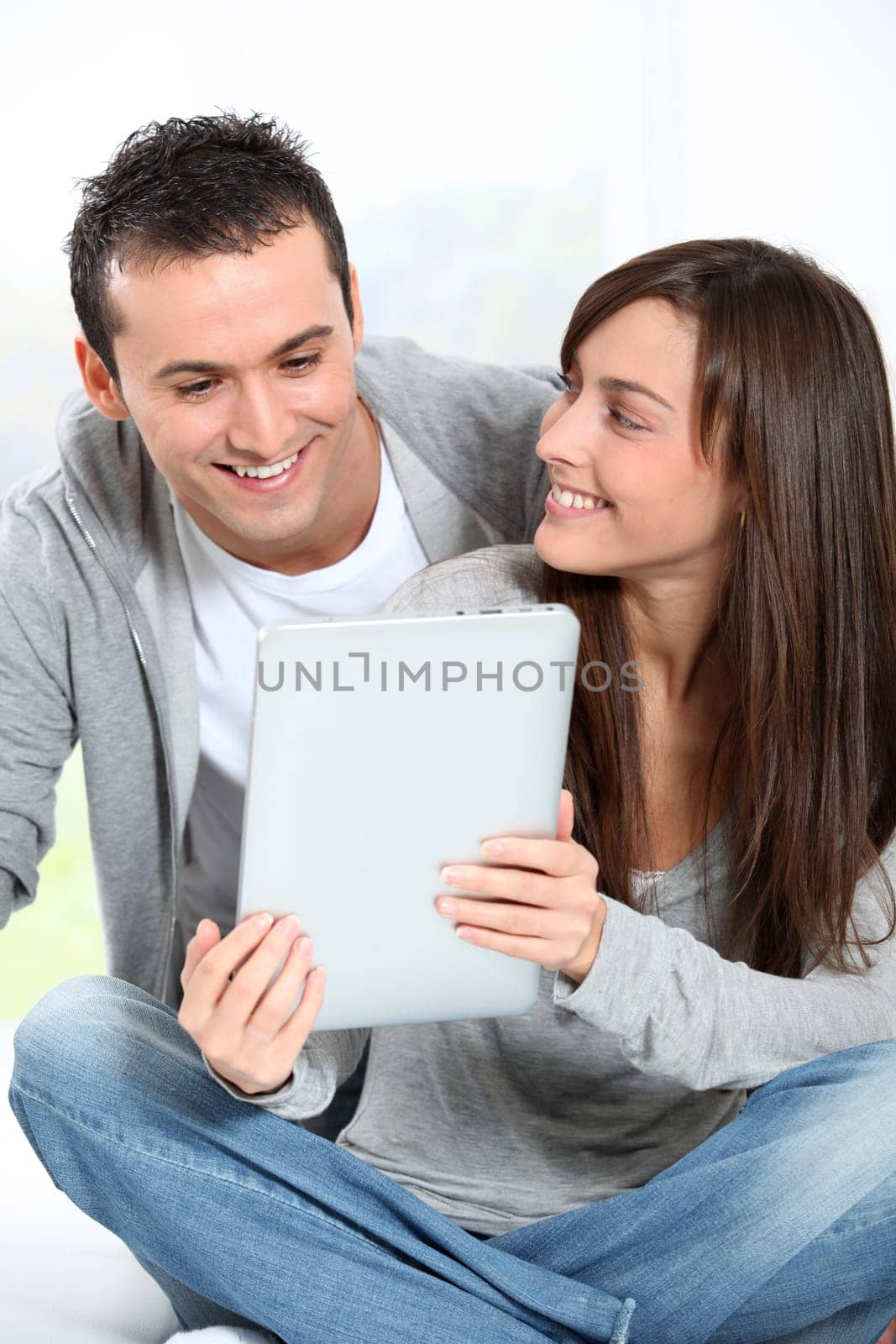 Young couple sitting on sofa with electronic pad