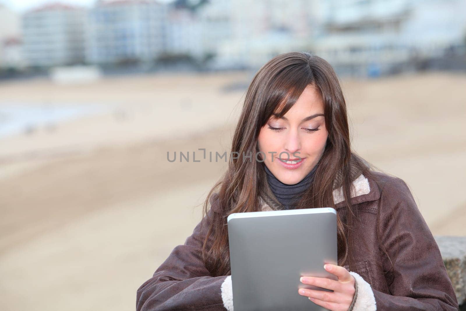 Young woman using electronic pad by the beach in winter