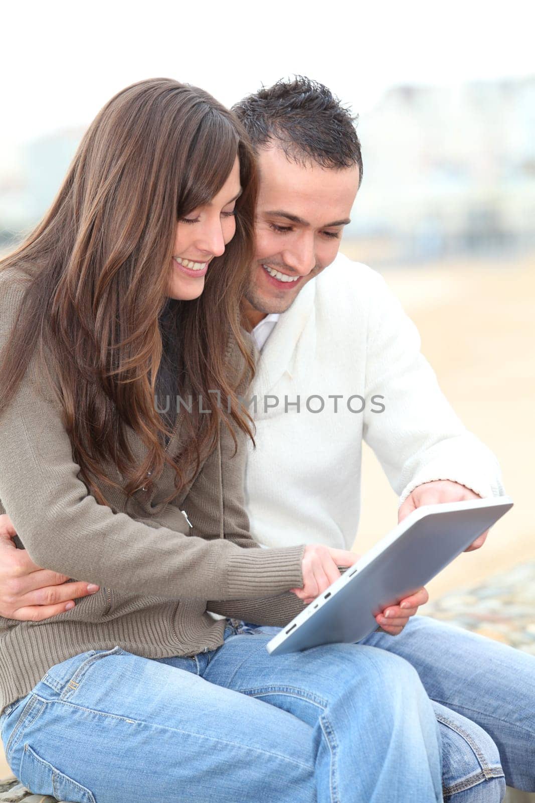 Young couple using electronic pad by the beach in winter