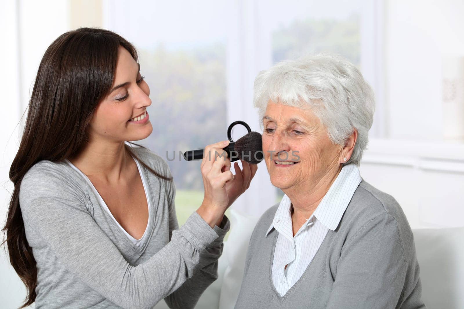 Young woman helping old woman to put makeup on