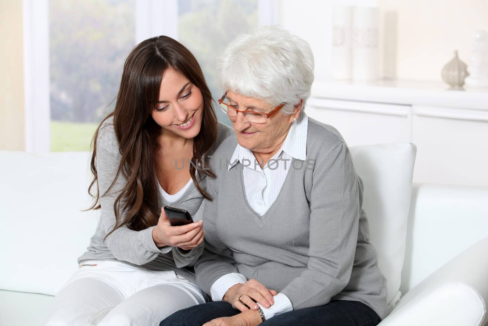 Young woman showing how to use mobile phone to grandmother