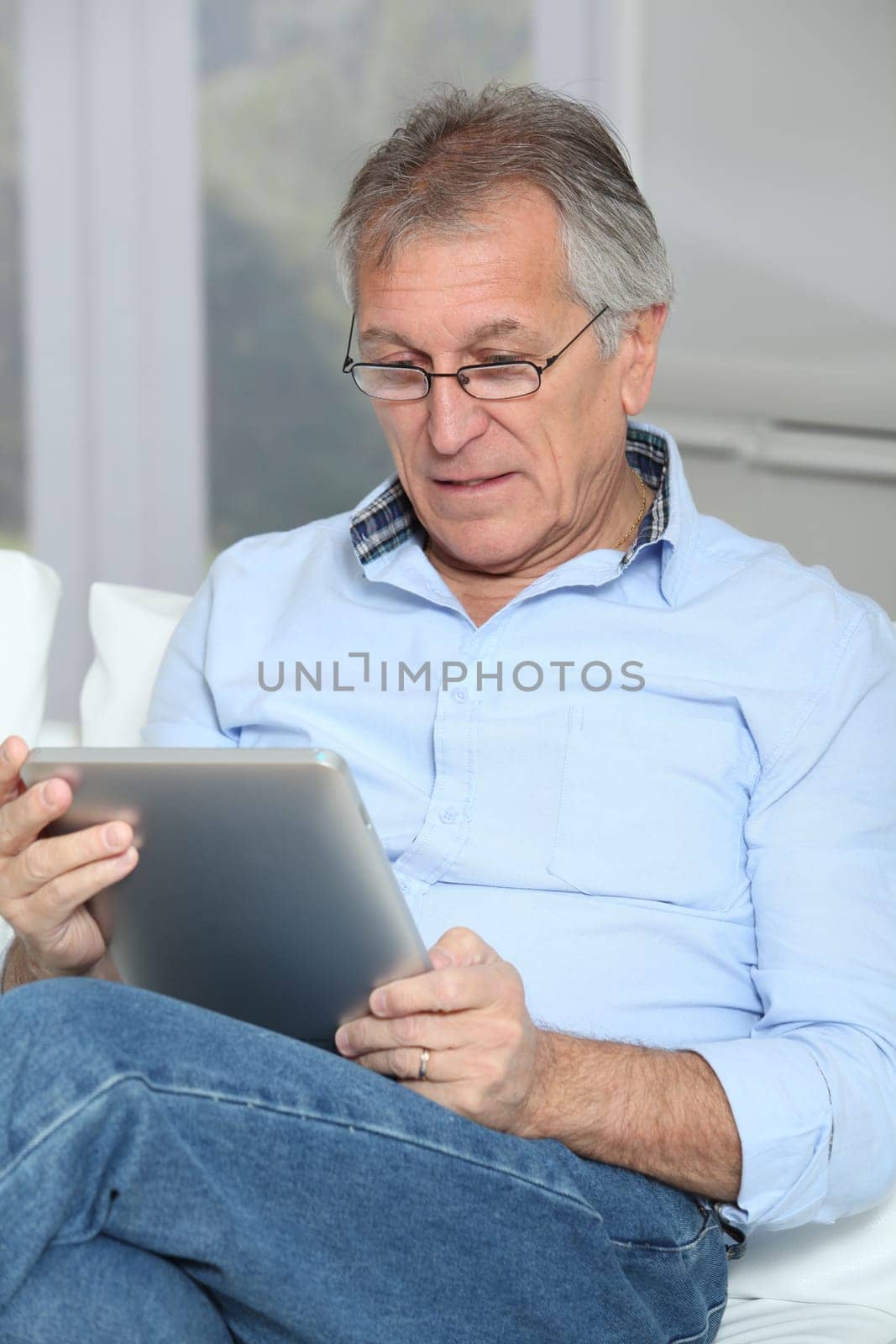 Senior man sitting in sofa with electronic tablet
