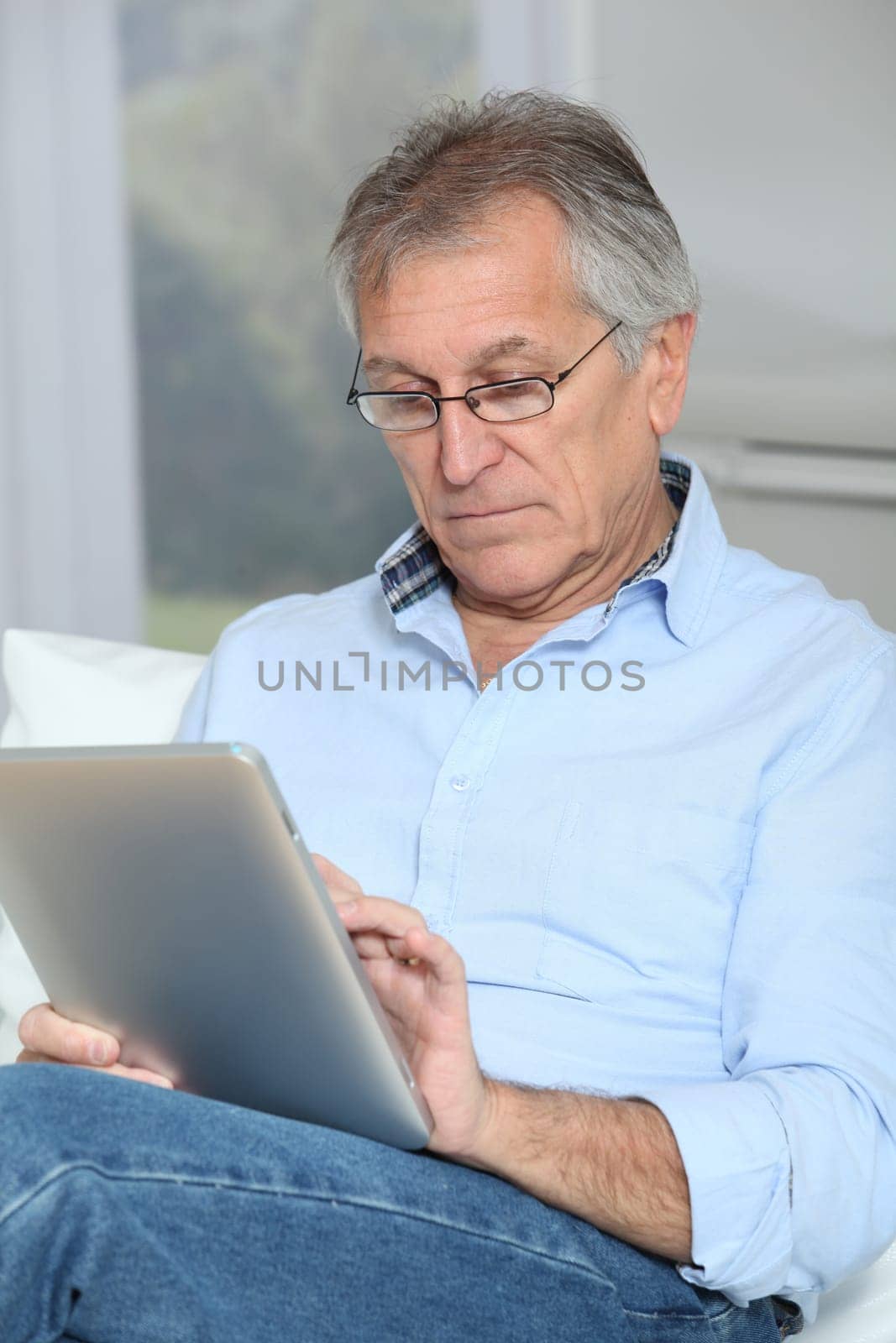 Senior man sitting in sofa with electronic tablet