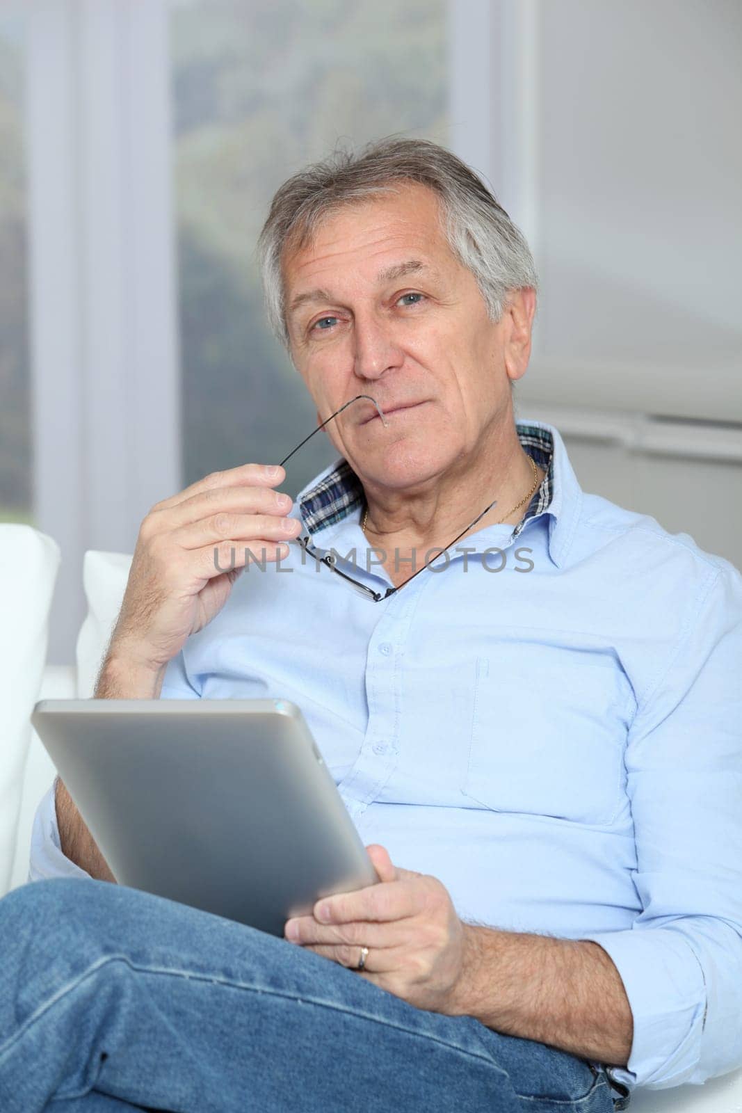 Senior man sitting in sofa with electronic tablet