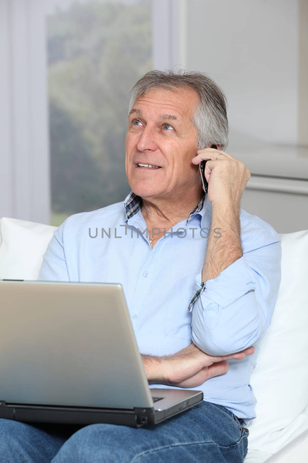 Senior man in sofa with laptop computer and mobile phone