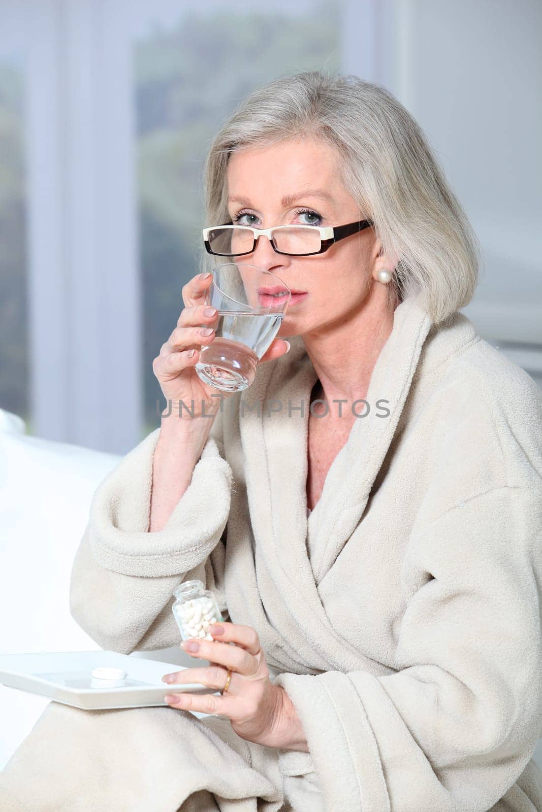 Senior woman in bathrobe taking pills