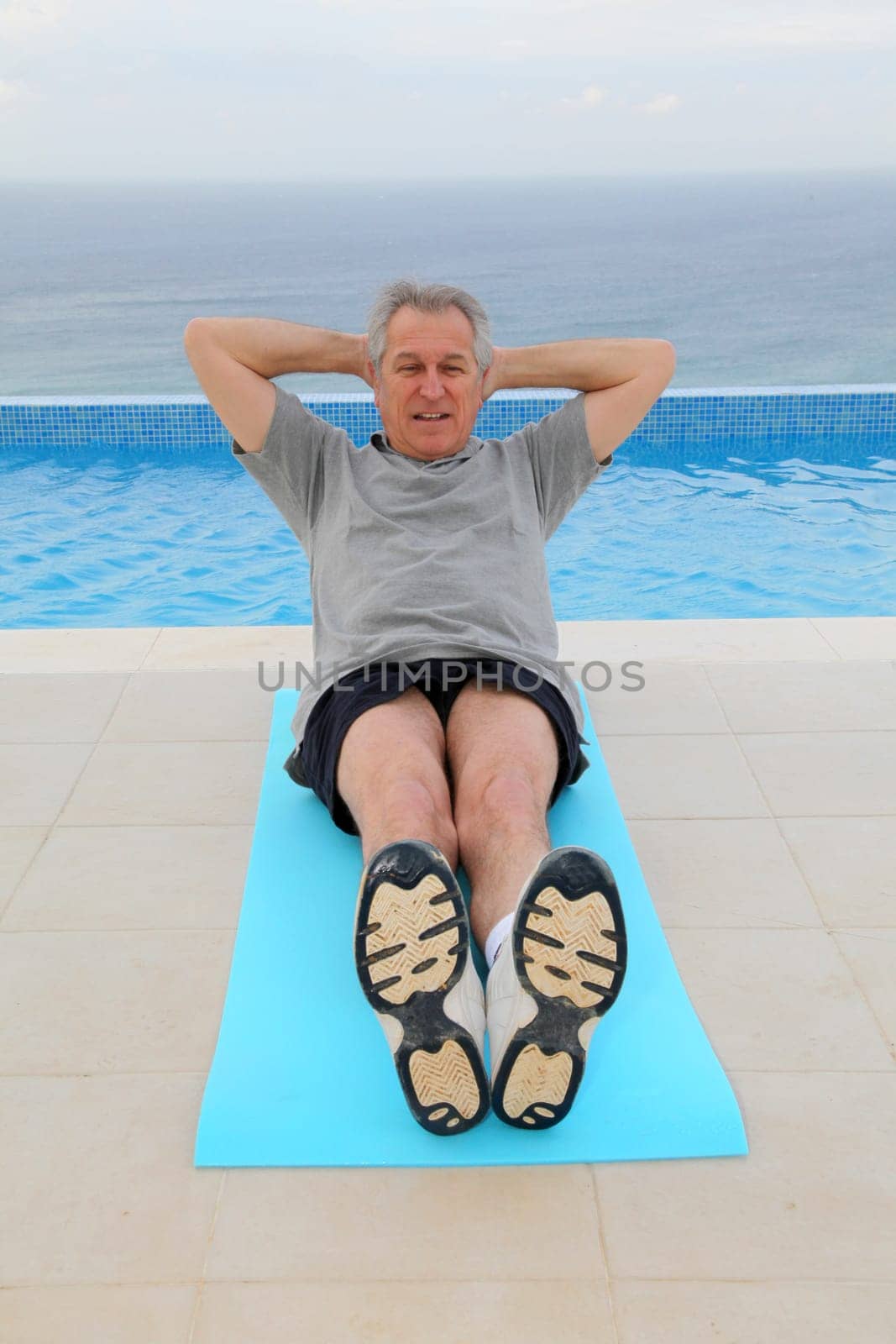 Senior man doing exercises by a swimming-pool