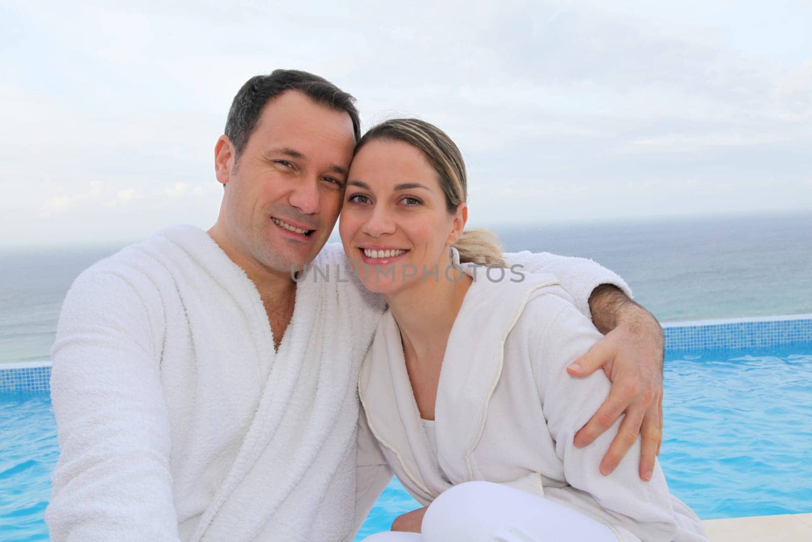Couple in bathrobe sitting by swimming-pool