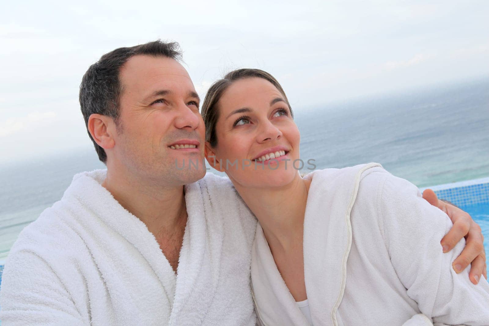 Couple in bathrobe sitting by swimming-pool
