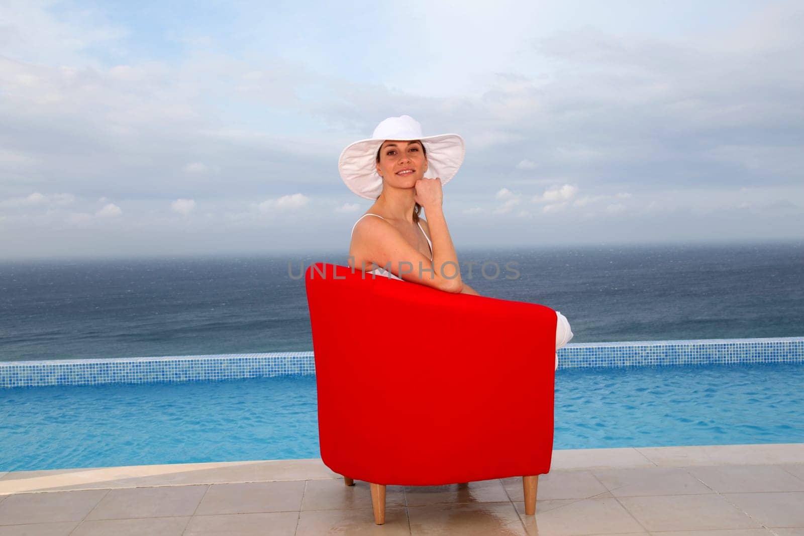 Beautiful woman relaxing in red chair by a swimming-pool