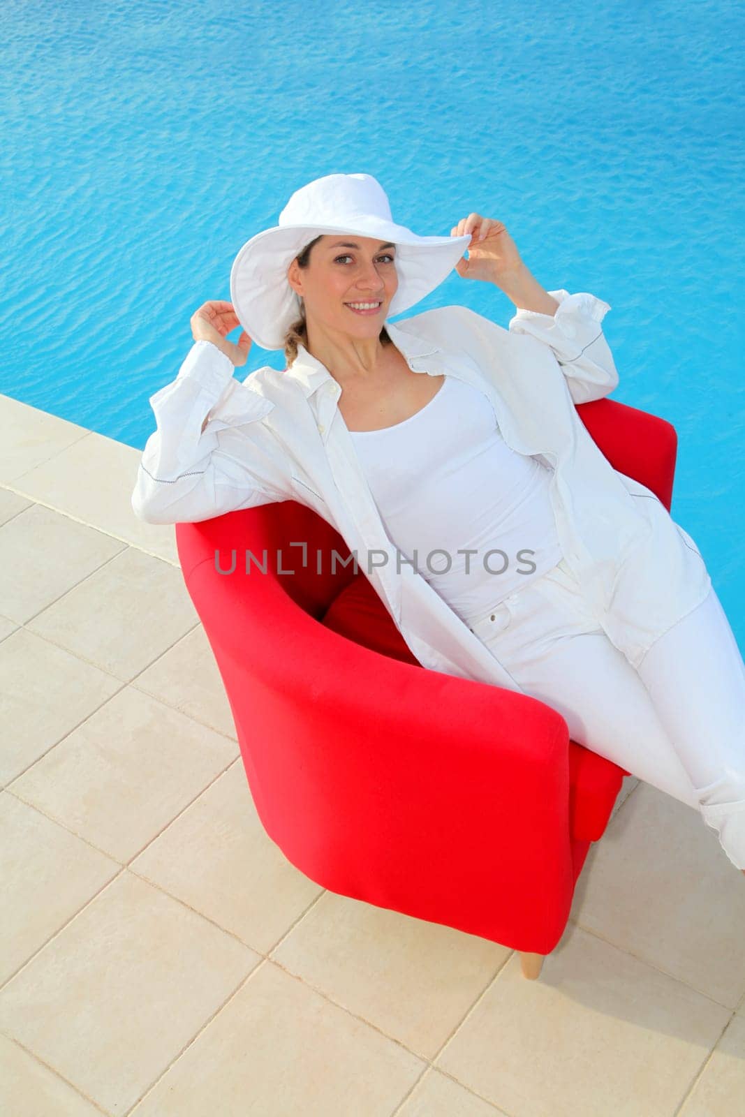 Beautiful woman relaxing in red chair by a swimming-pool