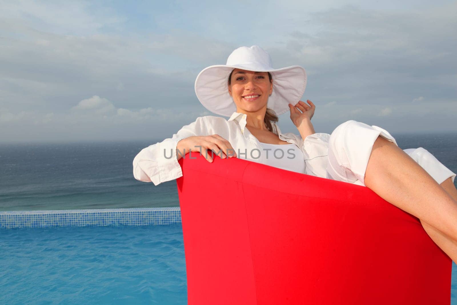 Beautiful woman relaxing in red chair by a swimming-pool