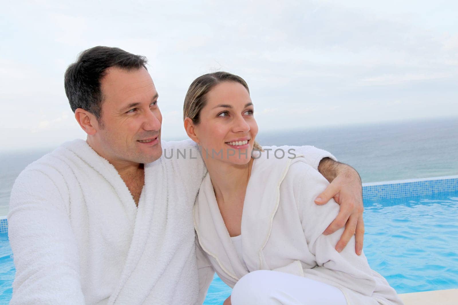 Couple in bathrobe sitting by swimming-pool