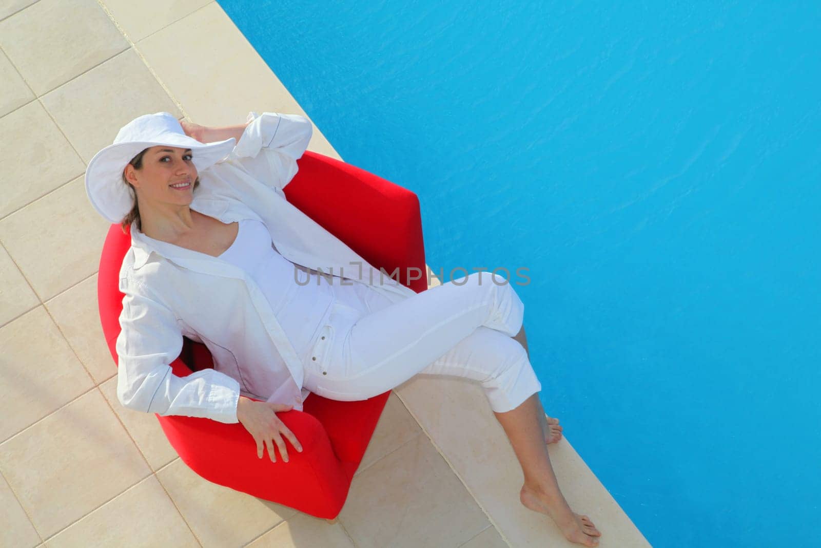 Beautiful woman relaxing in red chair by a swimming-pool