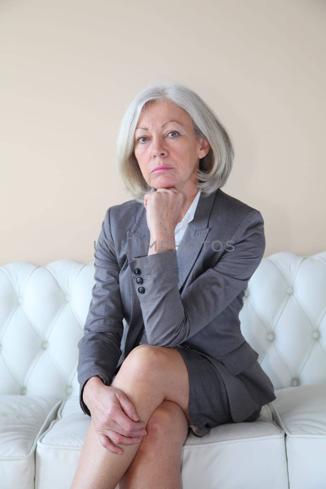 Senior woman in grey suit sitting in white sofa