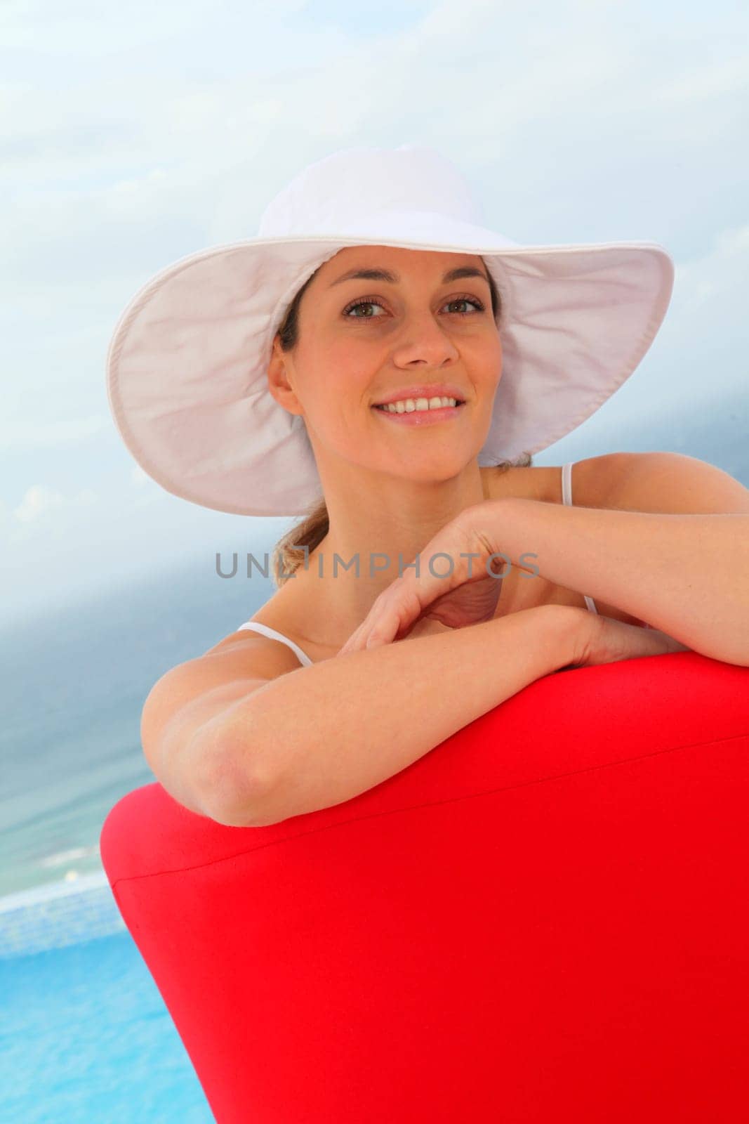 Beautiful woman relaxing in red chair by a swimming-pool