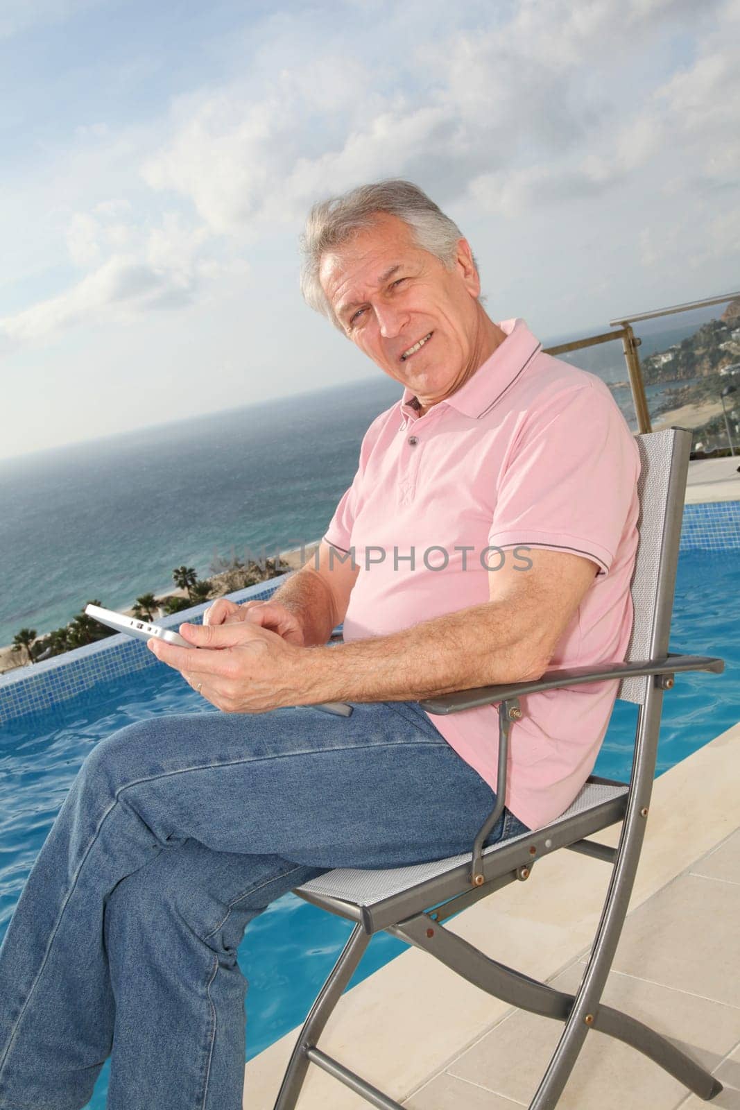 Senior man using electronic tablet by a swimming-pool