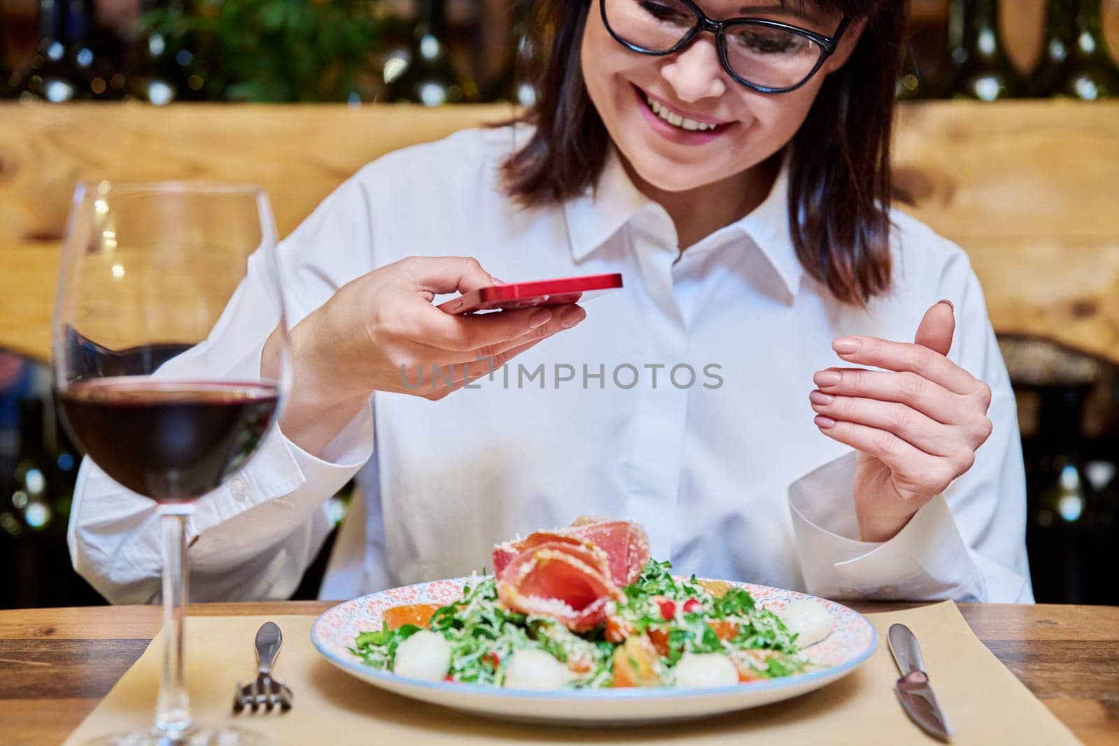 Happy woman in a restaurant taking pictures of food with a smartphone. Lifestyle, photo for social networks, personal blog concept