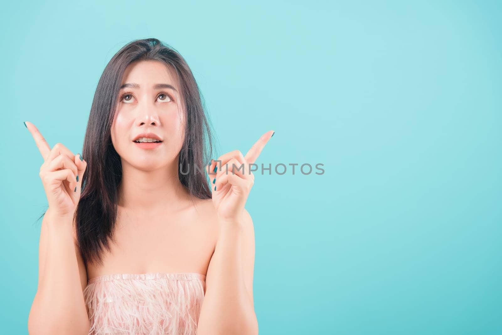 Asian happy portrait beautiful young woman standing her pointer finger up isolated on blue background with copy space for text