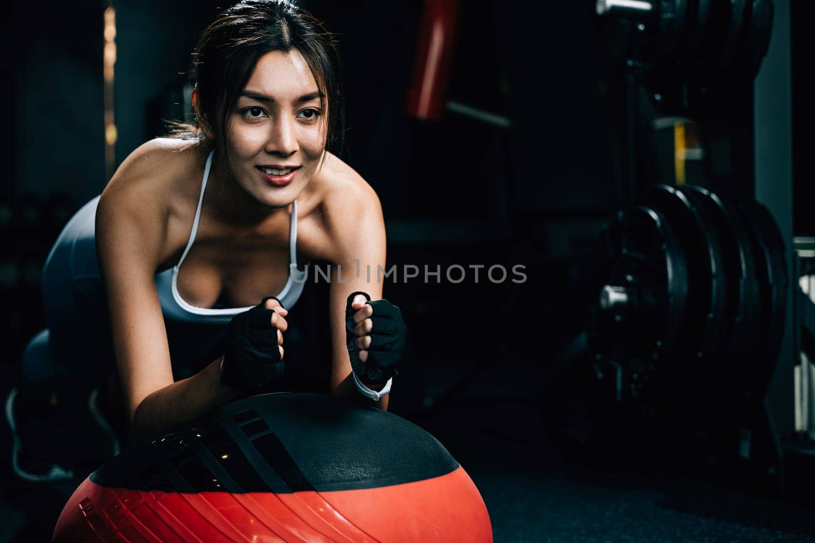 Young woman using a stability ball to challenge her plank position during an indoor gym workout, promoting strength and fitness care, exercise in dark gym background