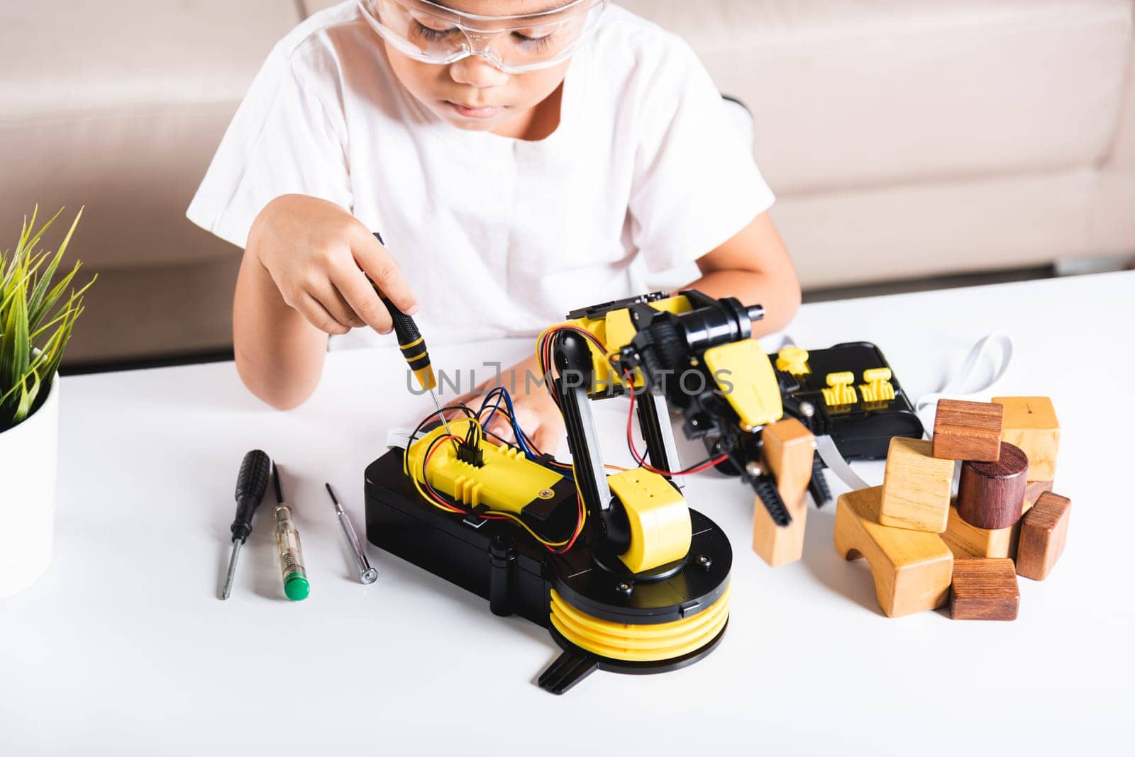 Happy Asian little kid boy using screwdriver to fixes screws robotic machine arm in home workshop, child learning repairing get lesson control robot arm, Technology future science education concept