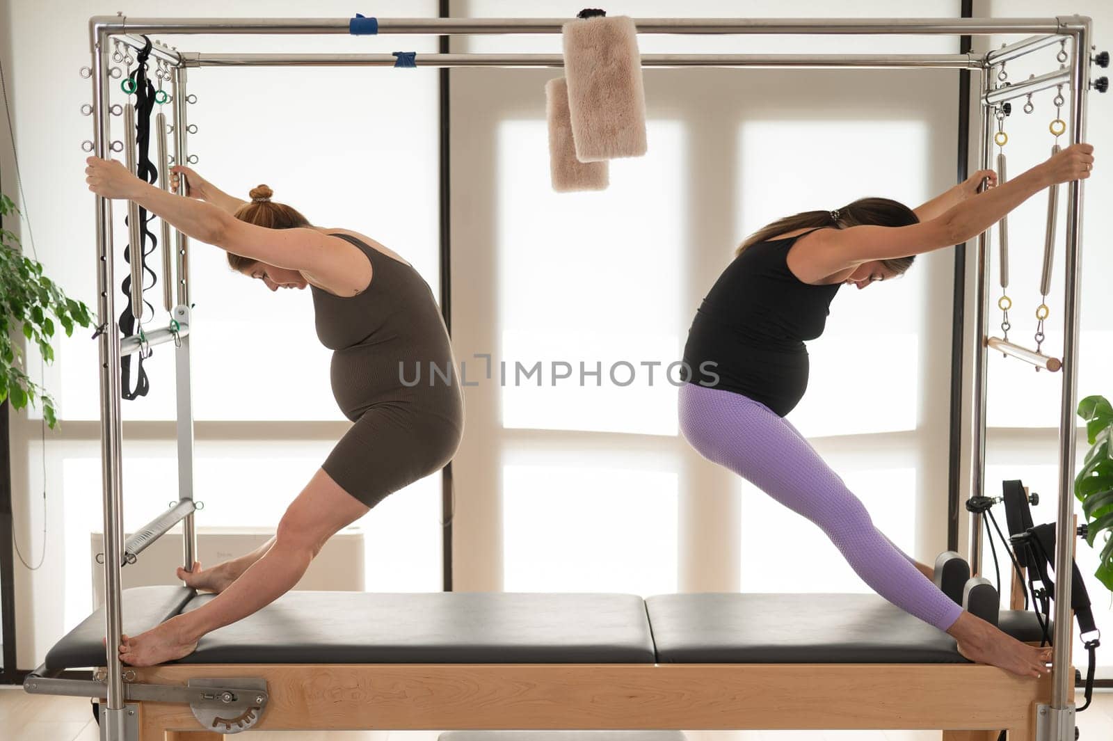 Two pregnant women are doing Pilates on a Cadillac reformer