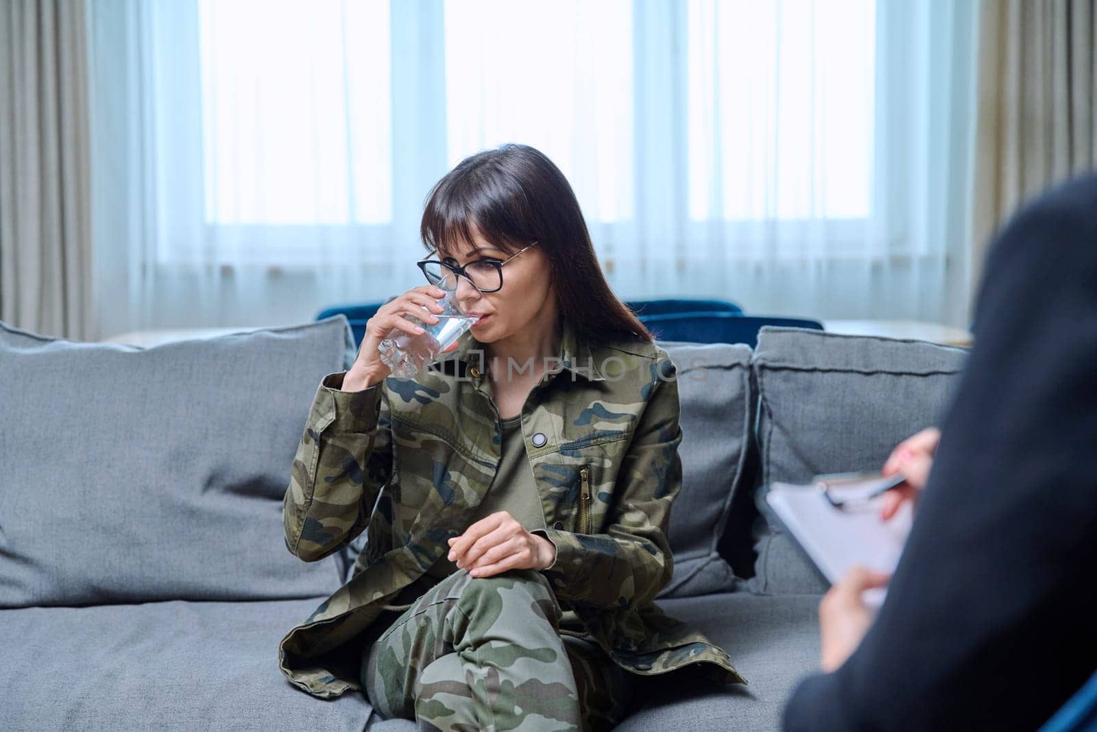 Middle-aged woman in military uniform at psychological therapy session in psychologist's office. Mental health treatment, professional help support, PTSD