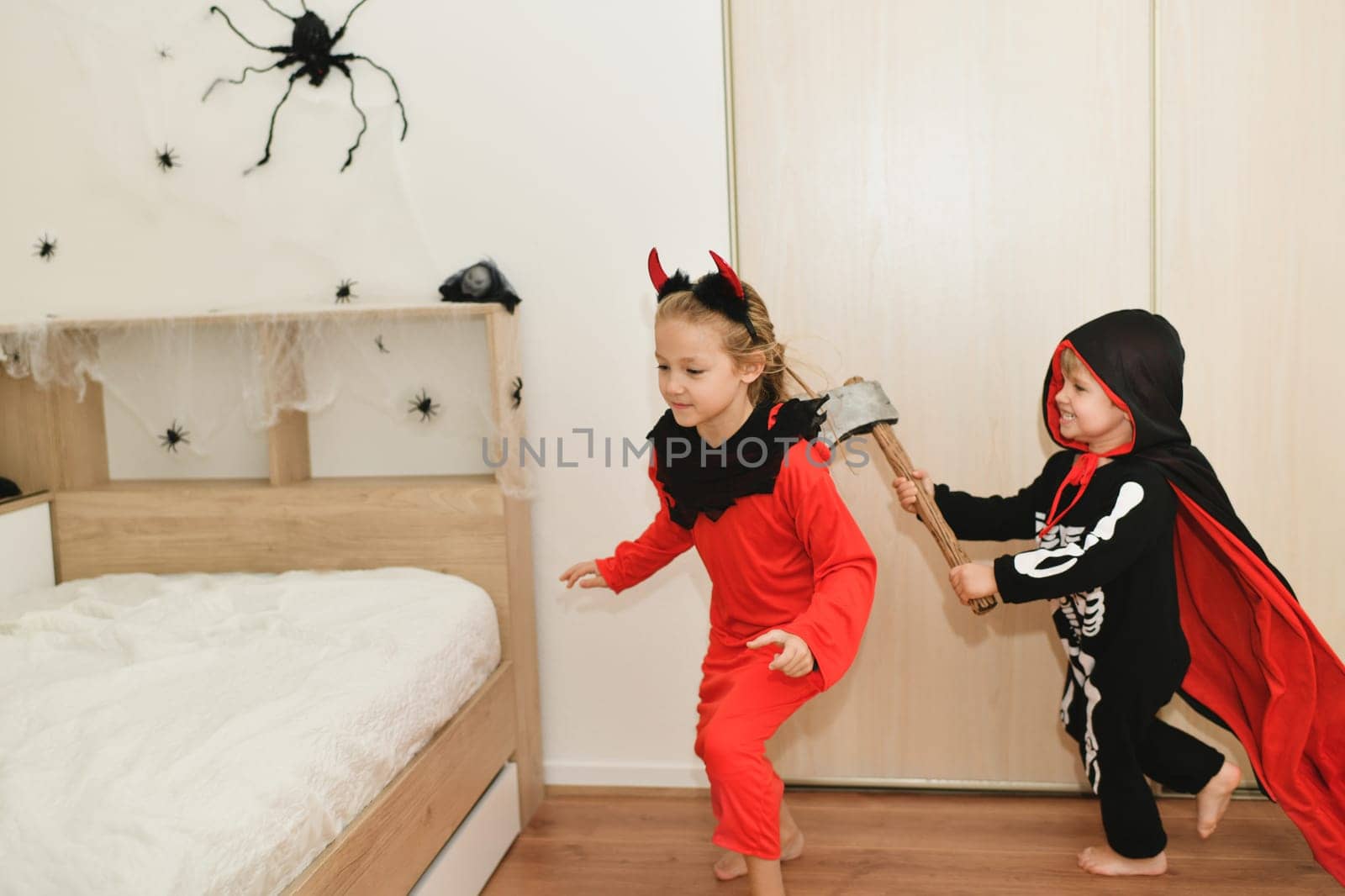 Children in skeleton and witch costume laughing at home by Godi