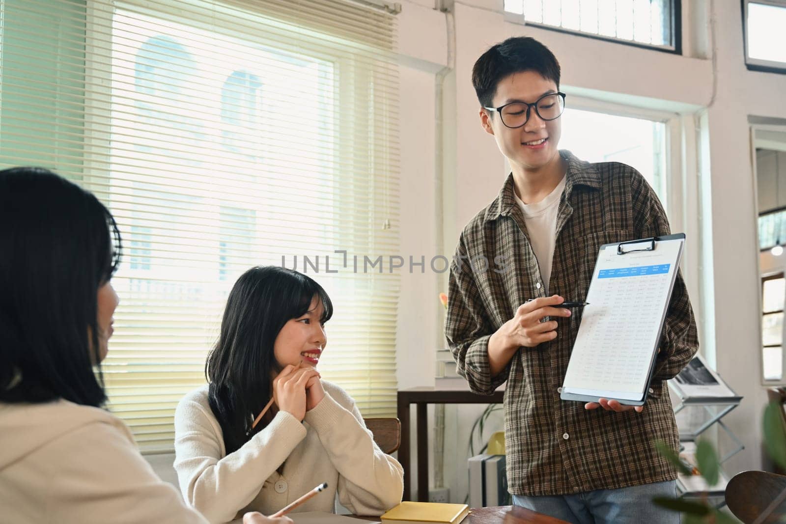 Confident man holding clipboard presenting idea, explaining plan, task to colleagues at meeting.