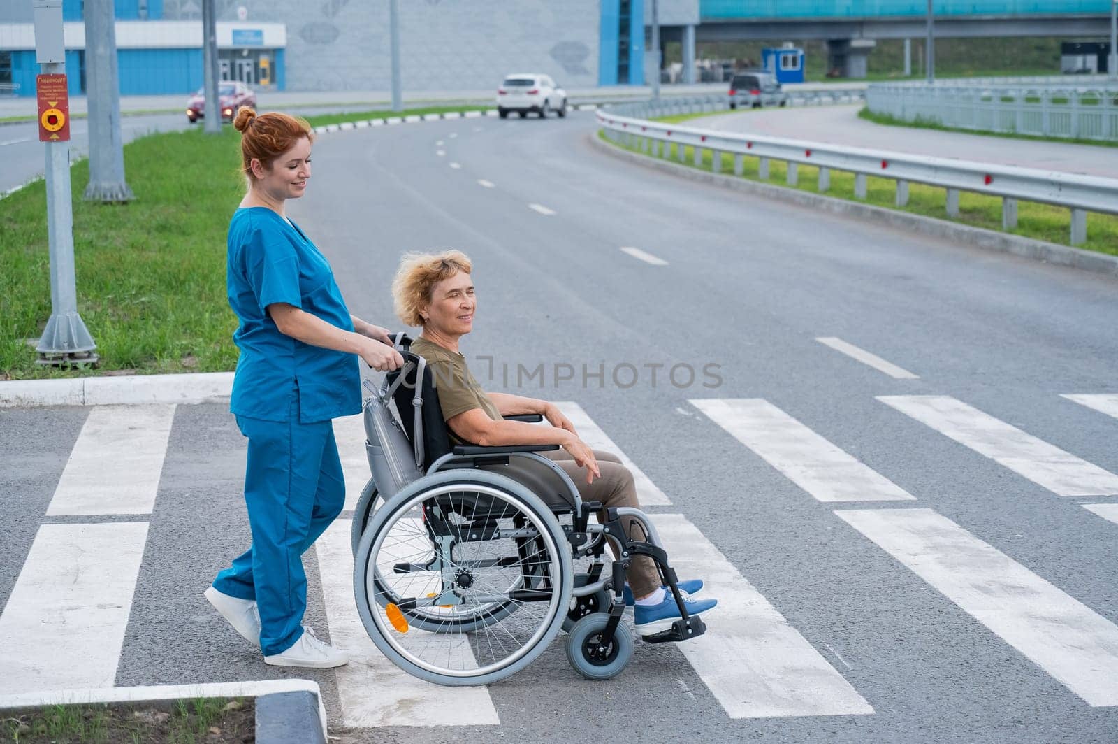 Profile of a nurse helping an elderly woman in a wheelchair cross the road
