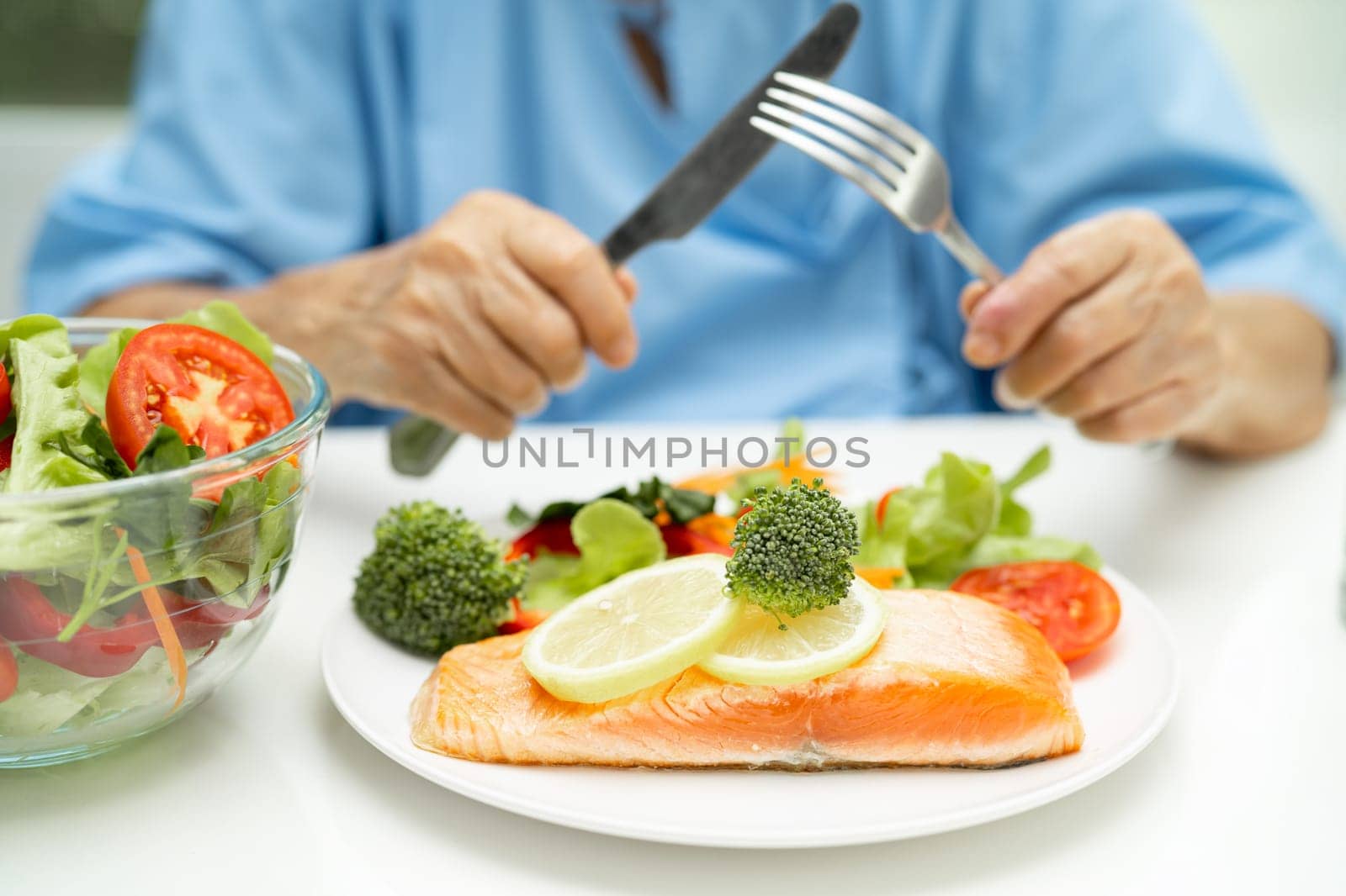 Asian elderly woman patient eating Salmon steak breakfast with vegetable healthy food while sitting and hungry on bed in hospital.