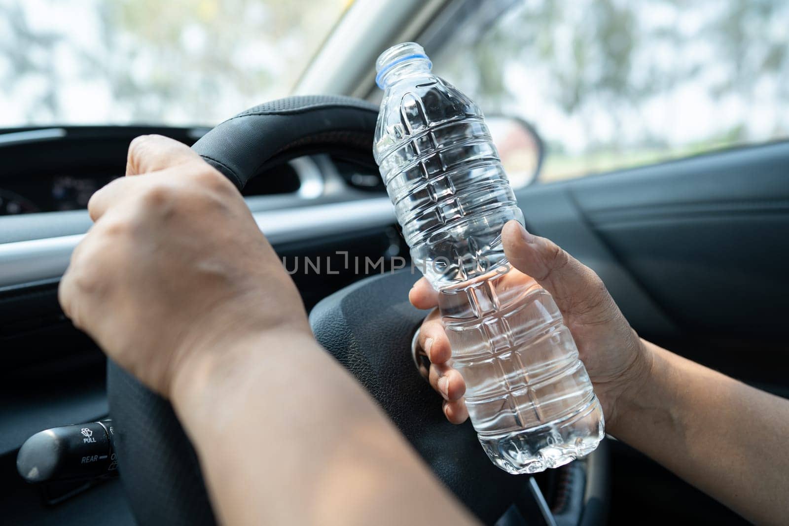 Asian woman driver holding bottle for drink water while driving a car. Plastic hot water bottle cause fire. by pamai