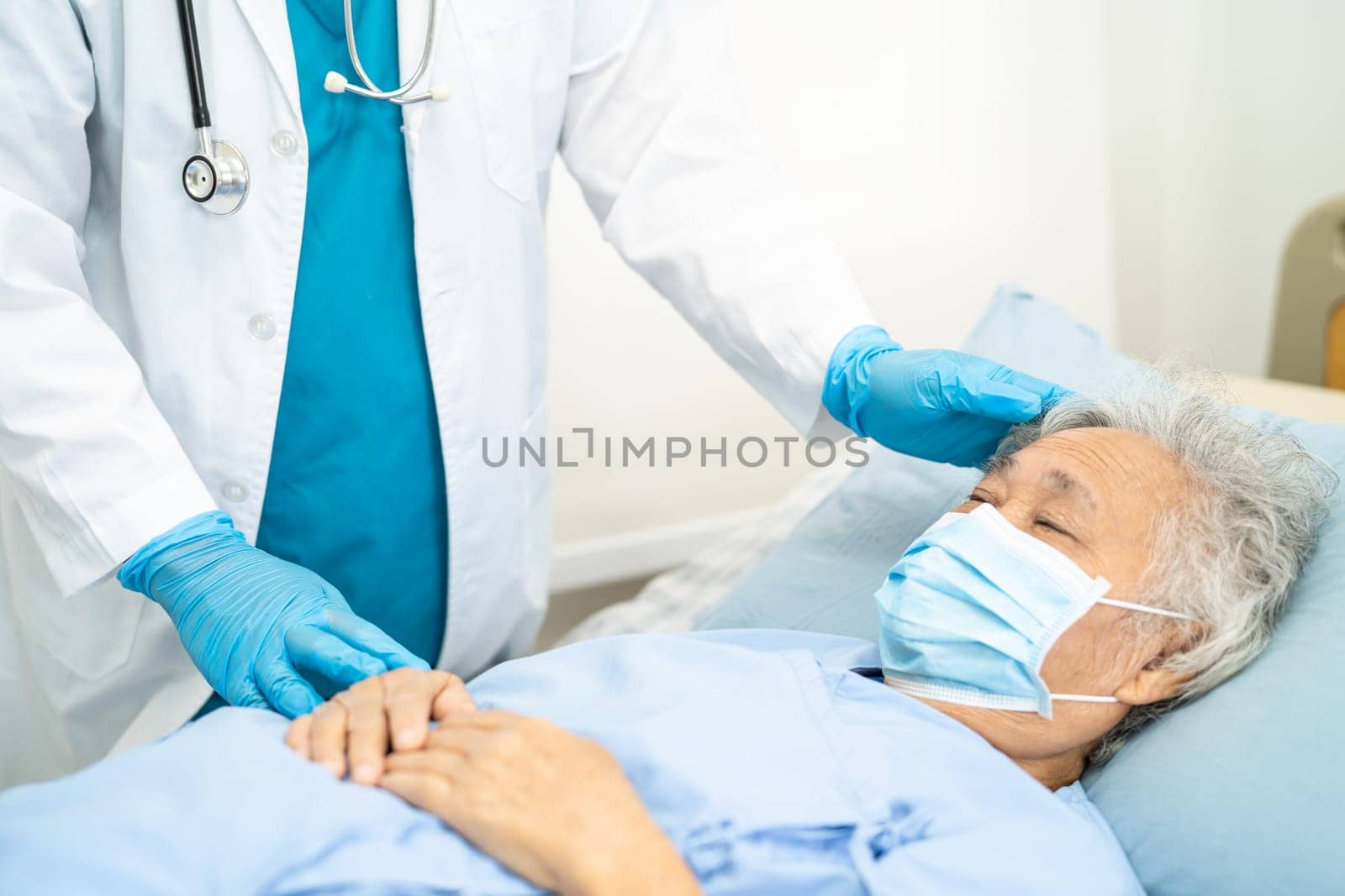 Doctor checking Asian senior woman patient wearing a face mask in hospital.