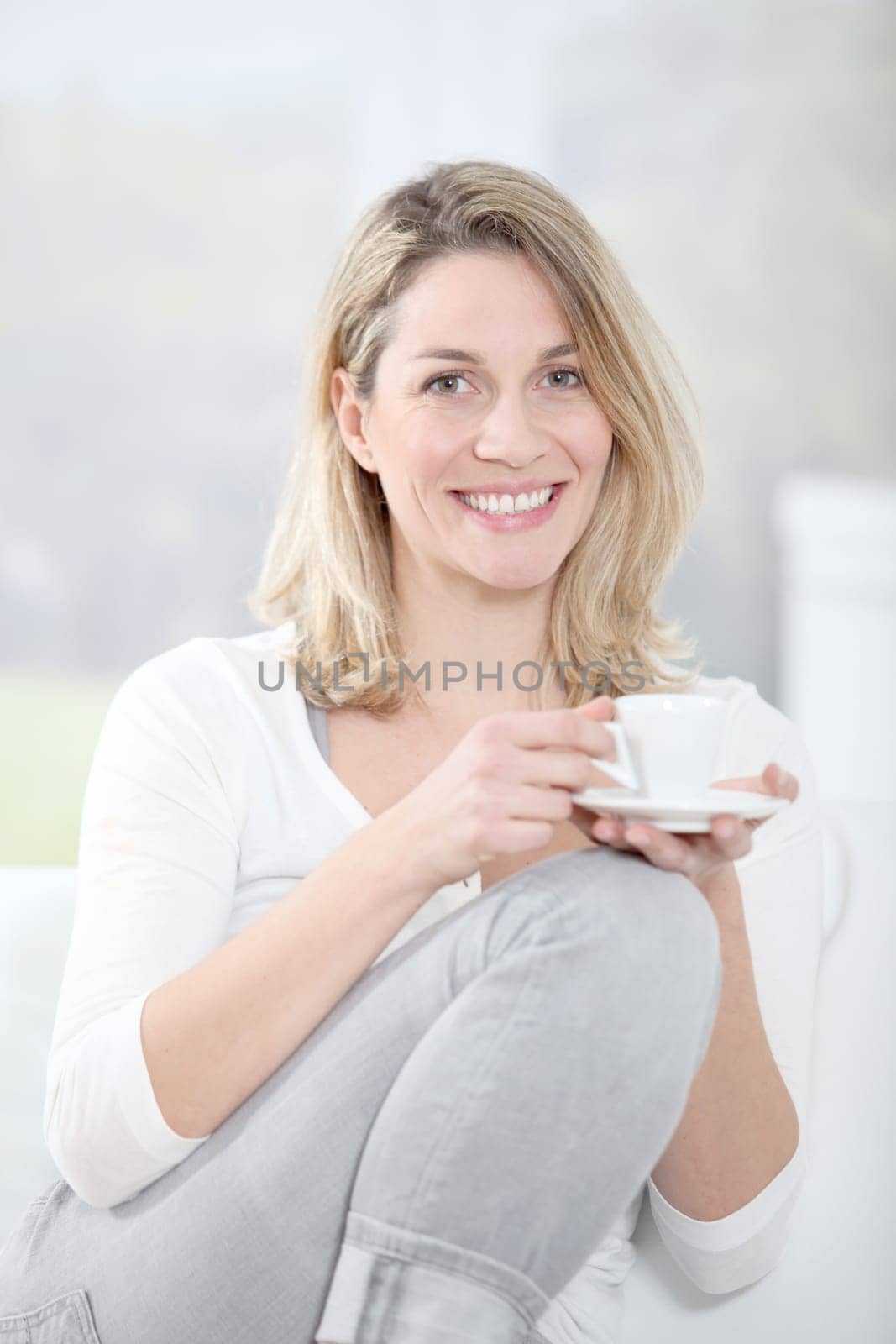 Blond woman in sofa holding coffee cup