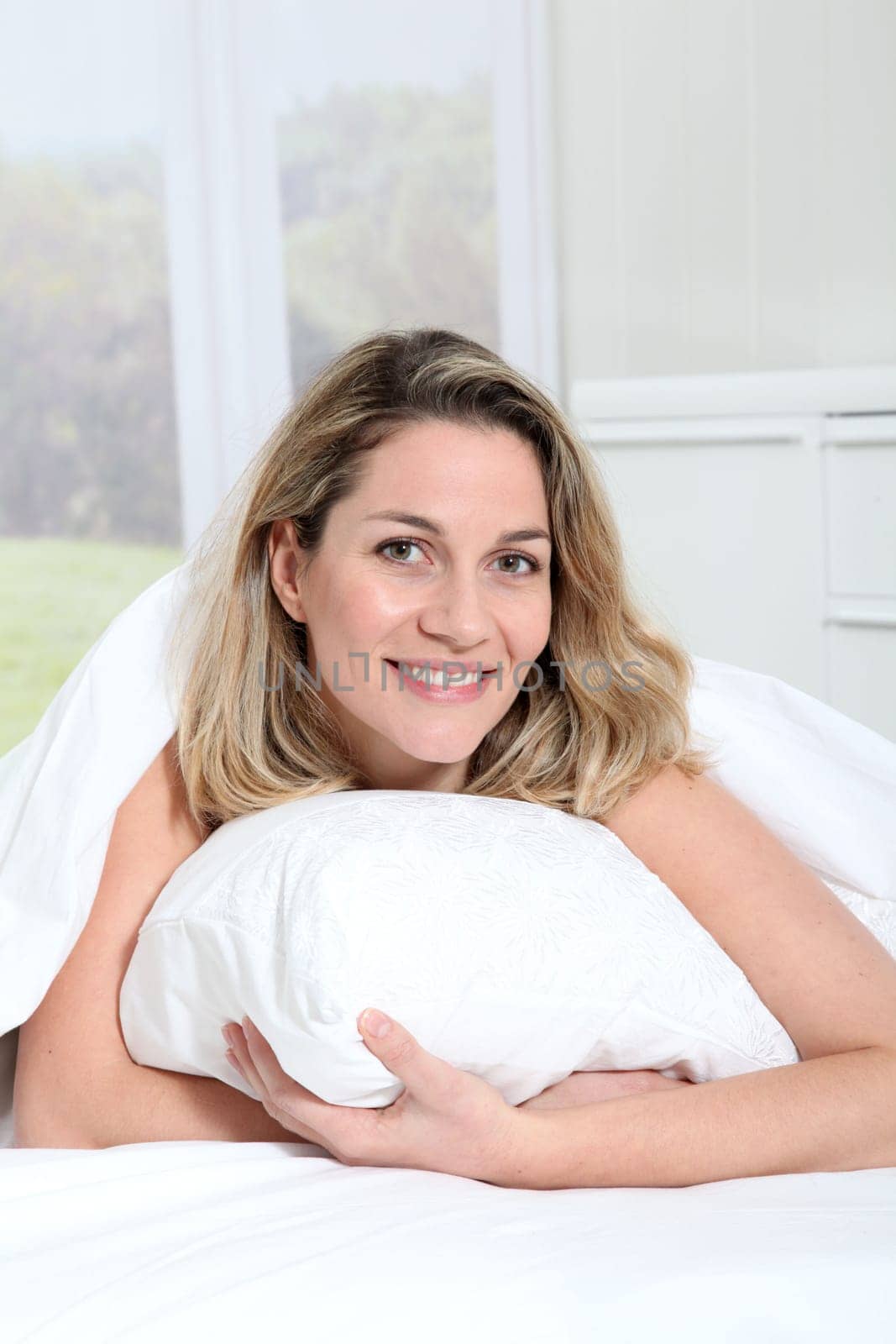 Portrait of beautiful blond woman laying in bed