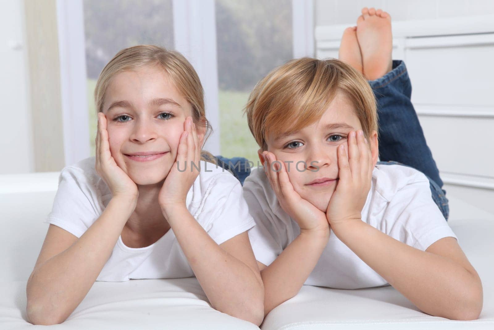 Blond children laying in sofa with hands on chin